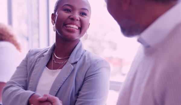 Woman in focus shaking hands with man in soft focus, view over the shoulder of the man on the left of the frame.