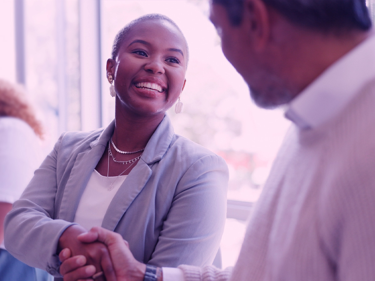 Woman in focus shaking hands with man in soft focus, view over the shoulder of the man on the left of the frame.