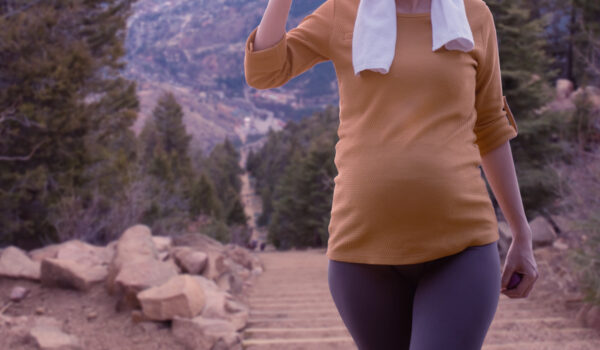 Pregnant woman hiking on a trail drinking from a water bottle.
