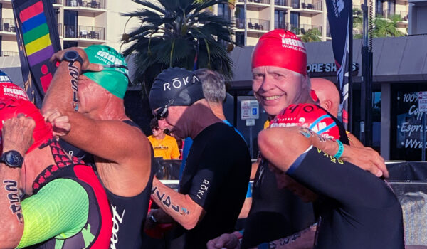 Dr. Leahy and a group of men queuing up in swimsuits and caps getting ready for the swimming portion of the Ironman competition.